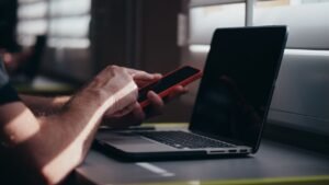 Home A person holding a smartphone near a laptop in an indoor setting, depicting modern technology use.